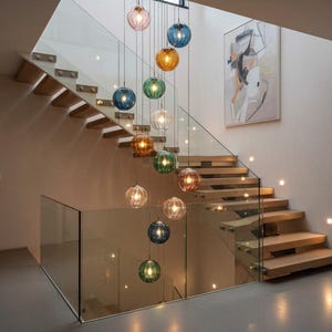 May include: A contemporary staircase with glass panels and wooden steps. A cascade of spherical pendant lights in various colours, including pink, blue, green, and amber, hangs from the ceiling, lighting the area. The staircase is a key design feature.
