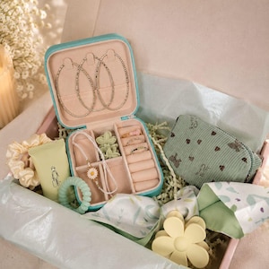 Könnte beinhalten: Eine Geschenkbox gefüllt mit Accessoires, darunter ein türkisfarbenes Schmuckkästchen mit Creolen, eine Halskette mit Gänseblümchen, Ringe, ein grünes Armband, eine kleine Geldbörse, ein Haargummi und eine gelbe Blumen-Haarspange. Die Box ist mit Seidenpapier und Dekopapier ausgekleidet.