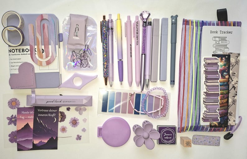 May include: A collection of lavender-themed stationery including a dotted notebook, washi tape, pens, a pencil case, sticky notes, a beaded bracelet, a flower-shaped hair clip, stickers, and a book tracker with a stack of books illustration.