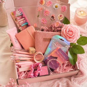 May include: A pink gift box filled with stationery and accessories. Items include a notebook, pens, stickers, a cosmetic bag, a candle, and a bracelet. The box is decorated with pink paper and a large pink rose.