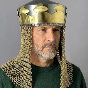 May include: A medieval-style helmet featuring a polished steel conical crown topped with a decorative brass band. The helmet includes a gold-toned chainmail aventail that drapes over the shoulders, constructed from interlocking metal rings.