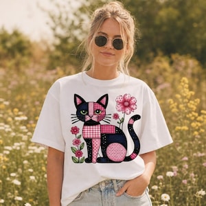 May include: A white t-shirt featuring a graphic of a cat composed of various pink, black, and white checkered and polka-dot patterns. The cat is positioned next to two pink flowers with green stems and leaves, rendered in a colorful, stylized design.