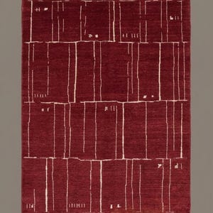 May include: A rectangular area rug in a deep burgundy red color featuring a geometric pattern of thin, off-white vertical lines and small rectangular blocks. The rug has a short, light-colored fringe along the top and bottom edges.
