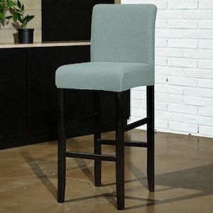 Könnte beinhalten: Ein hoher Barhocker mit hellblau-weiß karierter Sitzfläche und Rückenlehne. Der Hocker hat ein dunkelbraunes Holzgestell und Beine. Der Hocker steht vor einer weißen Backsteinmauer und einem schwarzen Schrank.