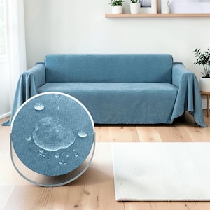 Puede incluir: Una funda de sofá azul drapeada sobre un sofá. La funda está hecha de una tela suave y texturizada. Un primer plano muestra agua formando gotas en la tela, lo que demuestra sus propiedades repelentes al agua. Una alfombra blanca está en el suelo.
