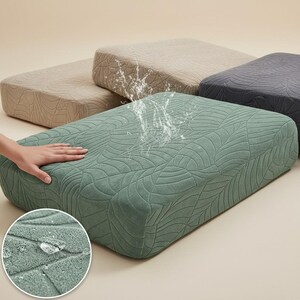 May include: Four rectangular cushion covers in shades of green, tan, and gray. The green cover is in the foreground, with a hand touching it. The covers have a leaf pattern and appear to be water-resistant.