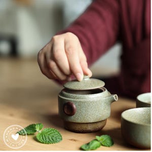 May include: A set of three ceramic mugs with a speckled, matte finish. The mugs are in shades of cream, light gray, and dark gray. Each mug has a simple, minimalist design and a rounded handle.