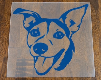 May include: A square, transparent adhesive decal featuring a dark blue, stylized graphic illustration of a dog's head. The dog is depicted with pointed ears, wide eyes, and an open mouth with its tongue hanging out in a cheerful expression.