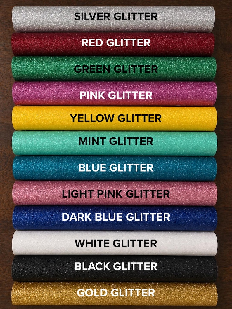 May include: A collection of twelve cylindrical rolls of glitter fabric arranged in a vertical stack. Each roll is labeled with its color: Silver, Red, Green, Pink, Yellow, Mint, Blue, Light Pink, Dark Blue, White, Black, and Gold Glitter.