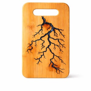 Op de afbeelding: Een rechthoekige bamboe snijplank met een handgreep. De plank heeft een donkerblauw bliksemontwerp. Het hout heeft een warme, natuurlijke tint en het ontwerp is gecentreerd.