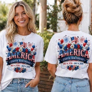 May include: White t-shirts with a patriotic design celebrating America's 250th birthday. The design includes the word "AMERICA" in red, white, and blue, along with flags, balloons, and the dates July 4, 1776 - July 4, 2026.
