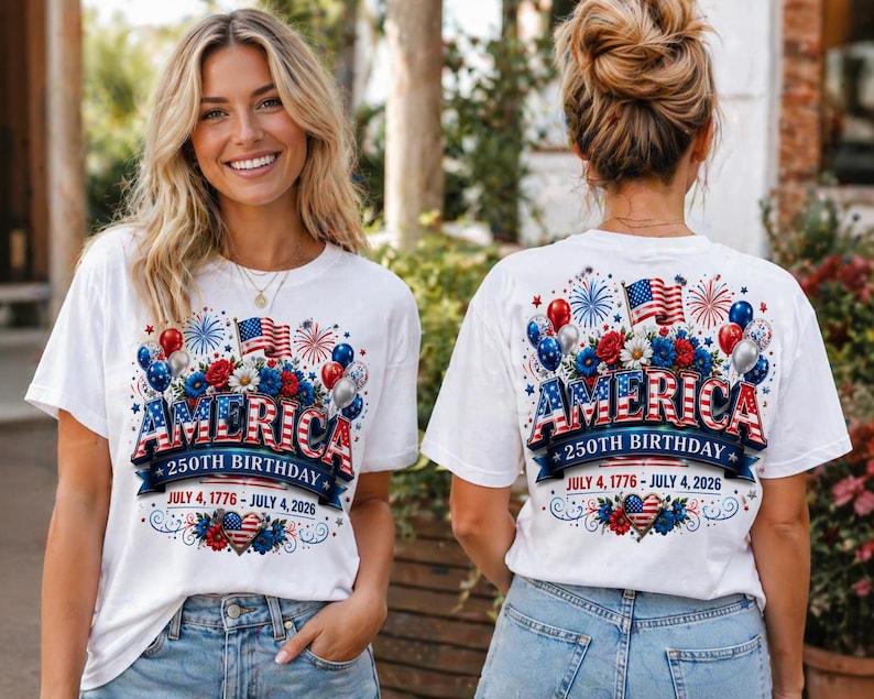 May include: White t-shirts with a patriotic design celebrating America's 250th birthday. The design includes the word "AMERICA" in red, white, and blue, along with flags, balloons, and the dates July 4, 1776 - July 4, 2026.