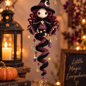 May include: A crocheted doll ornament featuring a figure with curly dark red hair, wearing a black pointed hat and a black and purple cape. The doll has a spiral tail in black and purple, decorated with gold-toned star and moon charms and purple beads.