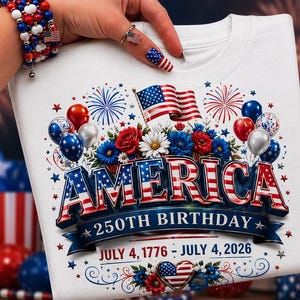 May include: White t-shirt with a patriotic design celebrating America's 250th birthday. The graphic features the word "AMERICA" in red, white, and blue, along with an American flag, flowers, balloons, and the dates July 4, 1776 - July 4, 2026.