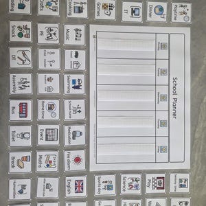 May include: A white school planner chart with five horizontal velcro strips for days of the week, accompanied by a collection of square cards featuring colourful icons and text labels for various school activities, subjects, and daily routines.