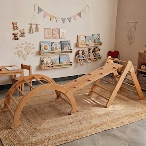 May include: A light wood children's play area with a climbing arch, a climbing triangle, and a slide. The room includes a small table and chairs, bookshelves with books and dolls, and decorative wall art. A woven rug covers the floor.