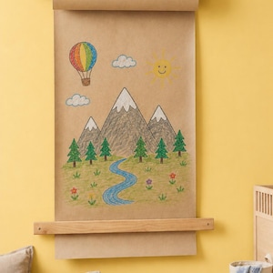 Pu&ograve; includere: Un dispenser di carta kraft marrone montato a parete con cinghie in pelle scura che sostiene un lungo foglio di carta con un disegno a pastello colorato di una mongolfiera, un sole sorridente, montagne innevate e un fiume blu.