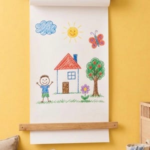 Pu&ograve; includere: Un dispenser di carta a parete con un'asta in legno sostenuta da cinghie in pelle scura. Un lungo foglio di carta bianca pende verso il basso, mostrando un disegno a matita colorata di una casa, una persona, un sole, una nuvola, una farfalla, un albero e un fiore.