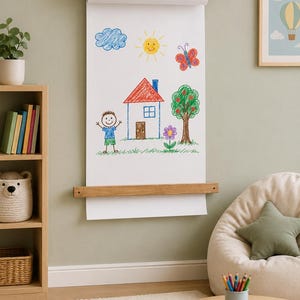 Pu&ograve; includere: Un dispenser di carta a parete realizzato in legno chiaro con cinghie in pelle, che sostiene un lungo foglio di carta bianca con un disegno a matita colorata raffigurante una casa, una persona, un albero, un sole, una nuvola, una farfalla e un fiore.