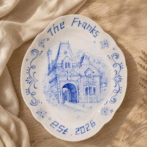 May include: An oval white ceramic platter with a scalloped edge, featuring a blue ink illustration of a house with an arched entryway. The text "The Franks" is printed at the top and "est. 2026" at the bottom, surrounded by blue floral motifs.