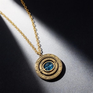 May include: A gold-colored pendant necklace with a blue gemstone center. The pendant has a circular design with geometric patterns and a chain. The necklace is displayed on a dark surface.