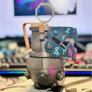 May include: A detailed, metallic replica of a grenade. The design features a light grey body with a wooden handle and accents. The top has a blue and teal design with symbols and the number 4 in pink. The grenade has a unique, stylized appearance.