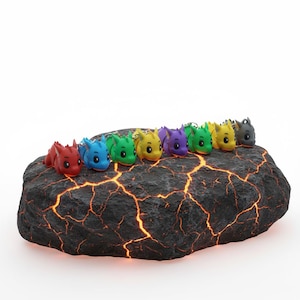 Może przedstawiać: Kolekcja kolorowych breloków w kształcie smoków w kolorach czerwonym, niebieskim, zielonym, żółtym, fioletowym i szarym. Figurki smoków ułożone są na ciemnej, teksturowanej skale z świecącymi pomarańczowymi pęknięciami. Każdy smok ma srebrny brelok.