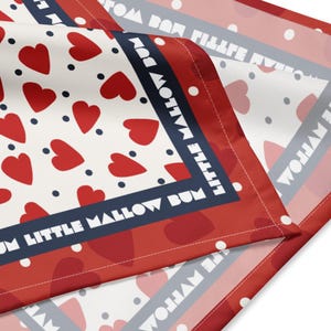 May include: A red, white, and blue patterned fabric with a repeating heart design. The fabric has a white background with red hearts and navy blue polka dots. The border features the text "LITTLE MALLOW BUM".