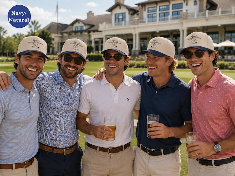 May include: A navy and natural colored baseball cap featuring a structured crown and a curved brim. The front panel displays a graphic of two crossed golf clubs with the text Ryan's Golf Weekend printed in a dark font above the clubs.