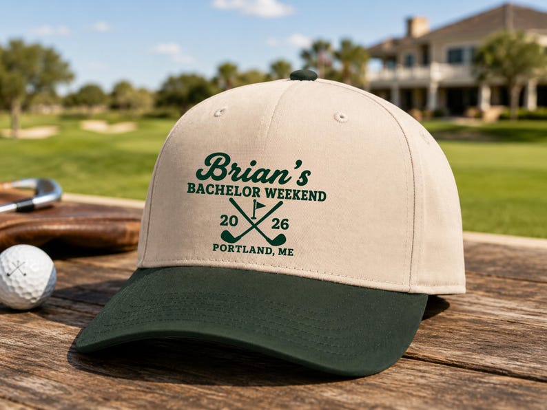 May include: A beige baseball cap with a dark green brim featuring dark green text that reads Brian's BACHELOR WEEKEND 20 26 PORTLAND, ME with a graphic of two crossed golf clubs and a flag centered on the front panel of the hat.