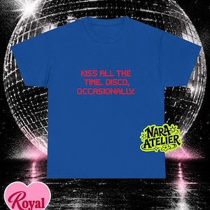 May include: A royal blue short-sleeve t-shirt featuring the red text "KISS ALL THE TIME. DISCO, OCCASIONALLY." centered on the chest. The shirt includes a small yellow logo in the bottom right corner that reads "NARA ATELIER" with a flower icon.