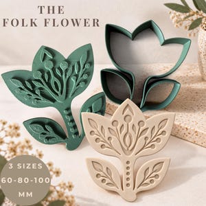 May include: Three folk flower cookie cutters in dark green and beige. One cutter is a dark green stamp, one is a beige stamp, and one is a dark green outline. Text reads THE FOLK FLOWER and 3 SIZES 60-80-100 MM. The cutters feature intricate floral designs.