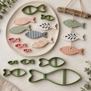 May include: A collection of fish-shaped items including green plastic cookie cutters in various sizes, ceramic fish ornaments hanging from a piece of driftwood, and flat ceramic fish tiles with patterns like stripes, scales, and leaves.