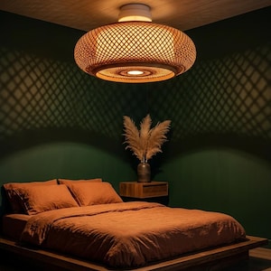 May include: A bedroom with a woven rattan pendant light. The light creates a diamond pattern on the dark green wall. The bed has orange bedding and a wooden frame. A vase of dried plants sits on a wooden bedside table.