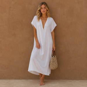 May include: A white, V-neck dress with lace trim. The dress is ankle-length and has short sleeves. A small, woven bag with brown leather handles is held in the hand.