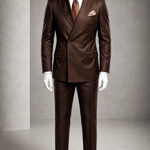 Puede incluir: Un traje cruzado de color marrón con camisa blanca, corbata marrón y pañuelo de bolsillo a juego. El texto TailoredTalesCrafts es visible en la parte superior. El traje se muestra en un maniquí con zapatos de vestir de cuero marrón oscuro.
