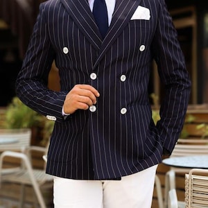 Może przedstawiać: Granatowa dwurzędowa marynarka w białe paski, zestawiona z białymi spodniami. Marynarka ma białe guziki i białą poszetkę. Tekst "TailoredTalesCrafts" jest widoczny u góry obrazu.