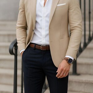 Pode incluir: Blazer bege com camisa branca, calças azul-marinho e cinto de couro castanho. Um relógio de couro castanho é visível no pulso. O texto "Tailored Tales Crafts" está no topo.