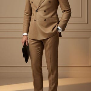 Puede incluir: Un traje marrón claro de doble botonadura con camisa blanca y corbata estampada. El traje incluye chaqueta y pantalón a juego, combinados con zapatos de cuero negro. También se ve un clutch negro. El texto "Tailored Tales Crafts" está en la parte superior.