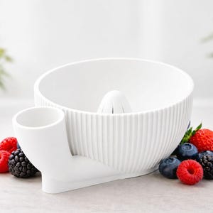 May include: A white citrus juicer with a ribbed bowl design and a built-in spout. Fresh blueberries, raspberries, blackberries, and a strawberry surround the juicer. The juicer is designed for easy use and efficient juice extraction.