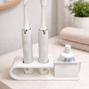 May include: A white electric toothbrush set with two toothbrushes, a holder, and a toothpaste tube. The toothbrushes are white with silver accents and a round button. The holder has two slots for the toothbrushes and a compartment for the toothpaste.
