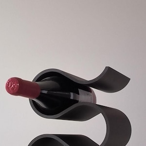 May include: A modern black wine rack with a unique, flowing design. The rack cradles a bottle of red wine, showcasing its label and the red wax seal. The rack's curves create an elegant display for a single bottle.