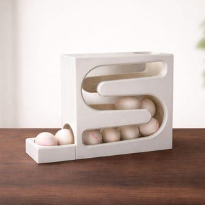 May include: A white wooden baseball dispenser with a unique S-shaped design. The dispenser holds several baseballs, some visible within the structure and others in a small tray. The baseballs have red stitching.