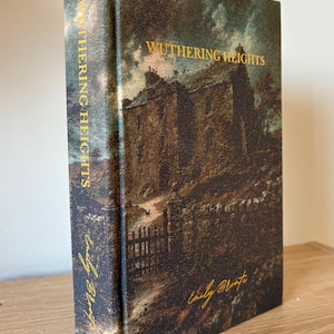 May include: A copy of "Wuthering Heights" by Emily Brontë. The book's cover displays a dark, evocative painting of a building and its surroundings. The title and author's name are in gold lettering.