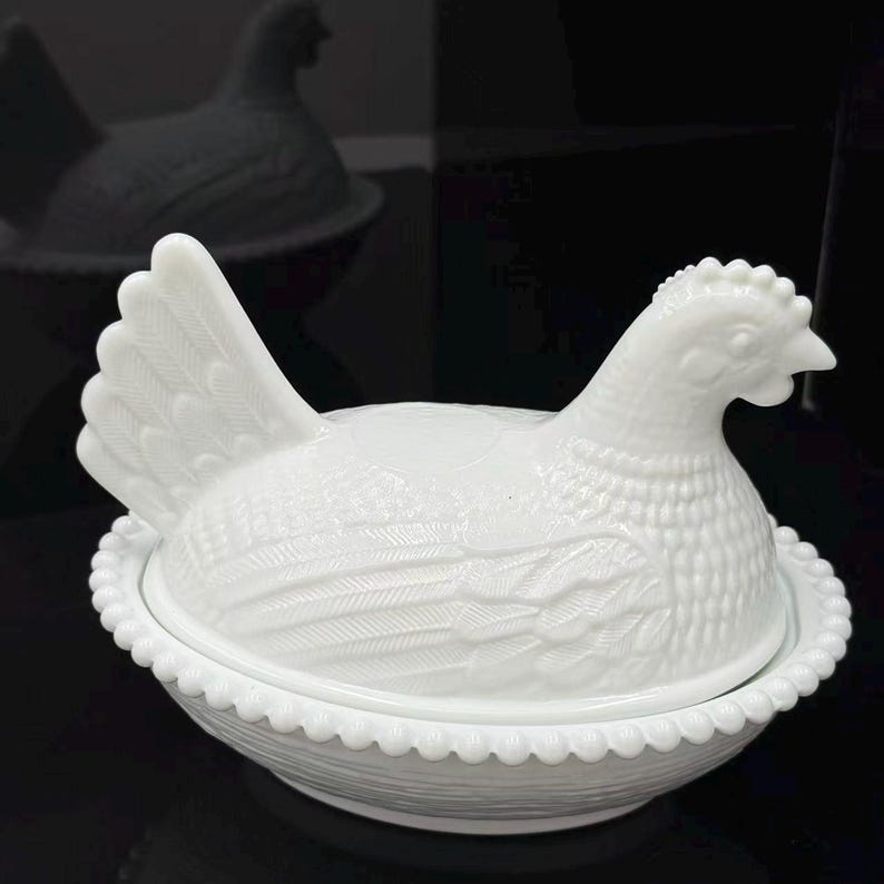 May include: A white milk glass hen on a nest dish. The lid is shaped like a sitting hen with detailed feather textures, and the base is a round bowl with a beaded rim and a woven basket pattern on the exterior, creating a classic lidded container.