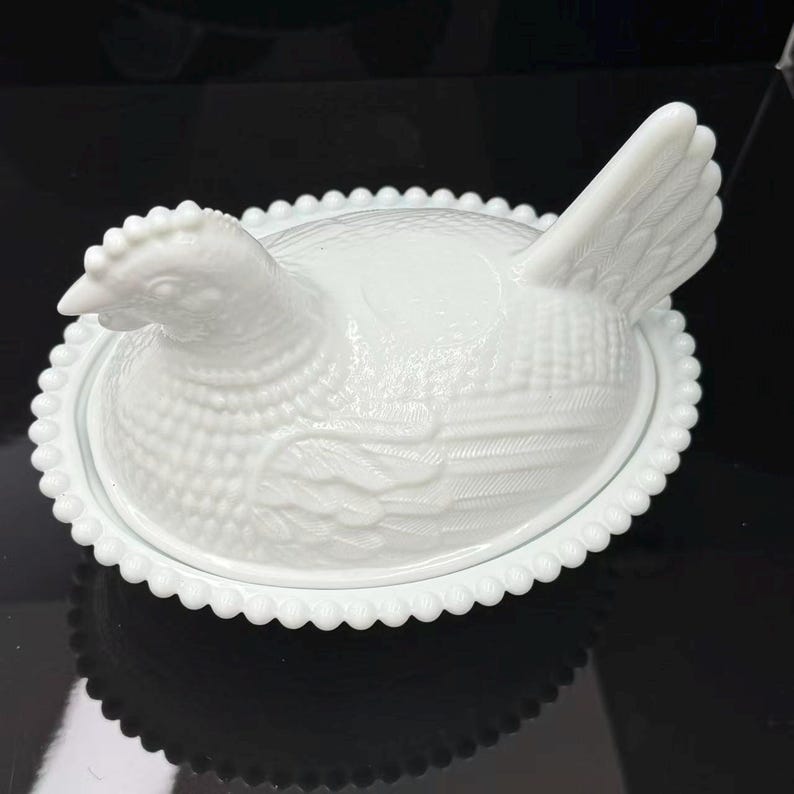 May include: A white milk glass hen on a nest dish featuring a detailed molded chicken figure with textured feathers and a comb, resting on an oval base with a decorative beaded edge. The lid is shaped like a sitting hen with a raised tail.