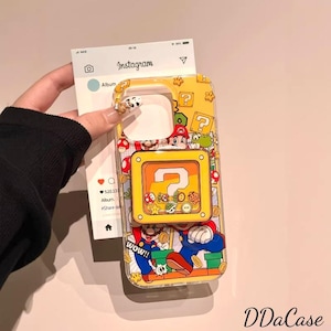 Puede incluir: Funda de teléfono amarilla con un diseño de Super Mario Bros. La funda presenta a Mario, bloques de interrogación y otros personajes del juego. La funda está sujeta por una persona.