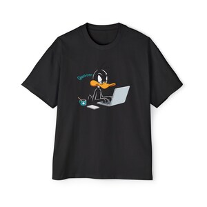 May include: Black t-shirt with a Daffy Duck cartoon design. The image shows Daffy Duck using a laptop, with a coffee cup and notepad. The text "Quack Off" is in a blue bubble. The shirt has a crew neck.