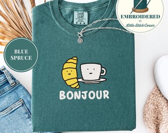 Camiseta Comfort Colors® bordada con el mensaje "Bonjour Croissant & Coffee", ideal para empezar el día con estilo o como regalo para amantes del café.