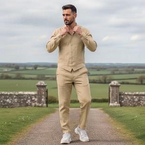 Puede incluir: Un traje de lino beige de tres piezas, que incluye una camisa de manga larga, un chaleco y un pantalón. El atuendo se combina con zapatillas blancas. El conjunto es adecuado para una ocasión informal o semiformal. El traje está hecho de tela ligera.